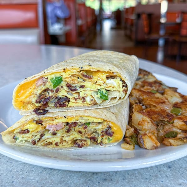 A breakfast burrito, cut in half, filled with eggs, bacon, cheese, and peppers, served with home fries.