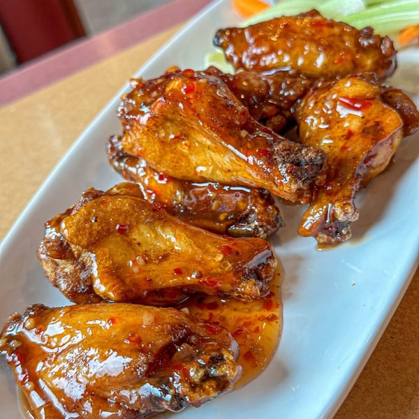 Sweet chili chicken wings, garnished with celery and carrot sticks, on a white rectangular plate.