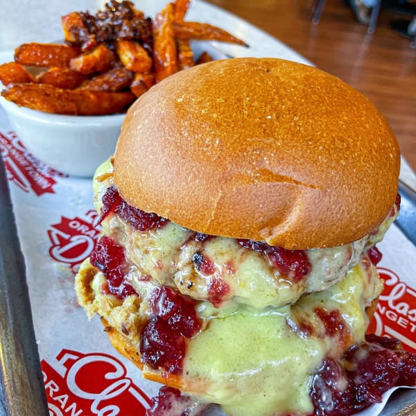 A Northvale Classic Diner burger with green sauce and cranberry, served with sweet potato fries.