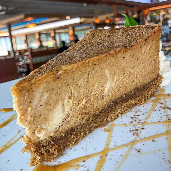 A slice of pumpkin cheesecake with a graham cracker crust, topped with cinnamon and caramel drizzle.