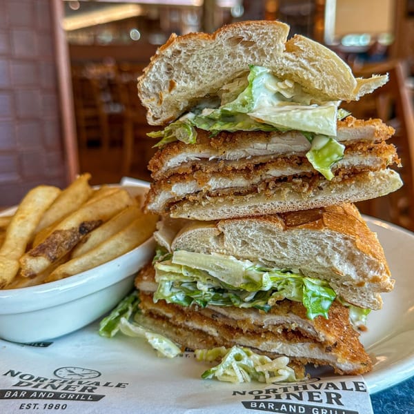 A large fried chicken sandwich with lettuce and sauce, served with a side of fries.