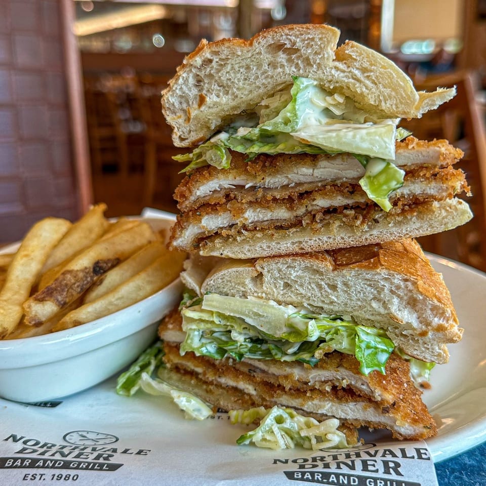 A large fried chicken sandwich with lettuce and sauce, served with a side of fries.