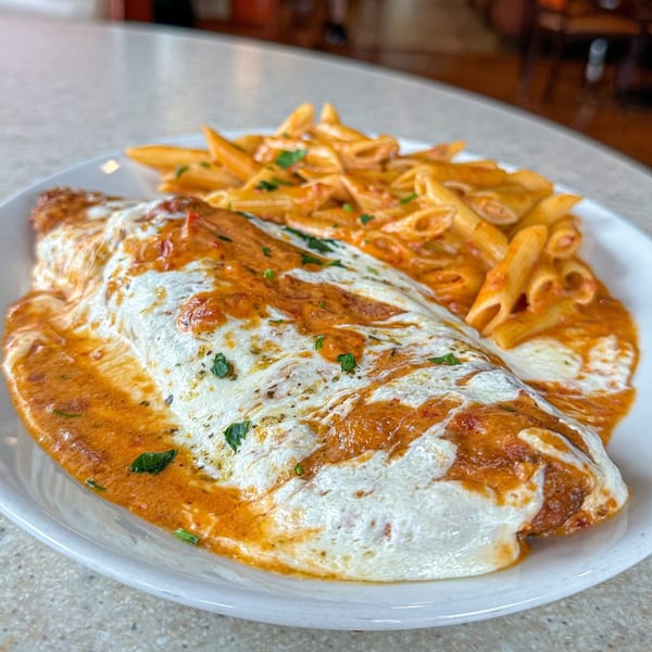 Chicken parmesan with penne pasta in a creamy tomato sauce, garnished with fresh herbs.