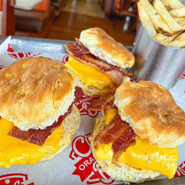 Three bacon, egg, and cheese biscuits on a tray with a side of french fries.