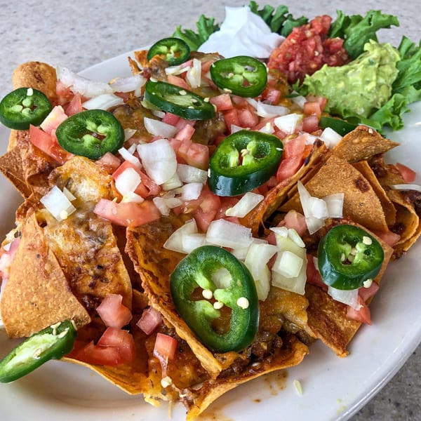 A plate of nachos with melted cheese, ground beef, diced tomatoes, onions, and jalapeños.